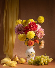 Bright bouquet of flowers in a white porcelain vase. Fruit on the table: a bunch of grapes, two pears. Yellow, red, orange dahlias. Useful products. Autumn still life.