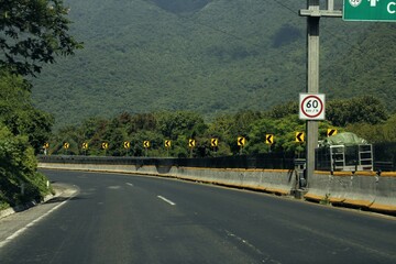 Autopista asfaltada con muro de contención con señalizaciones de transito y monte verde de fondo...