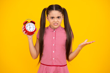 Unhappy sad teenager girl. Child holding clock over yellow background. Early morning, daily...