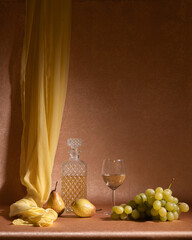 Fresh fruits on the table: two yellow pears, a bunch of grapes. Decanter, bottle of white wine. Glass of wine. Yellow curtain and orange background. Calm. Good mood.
