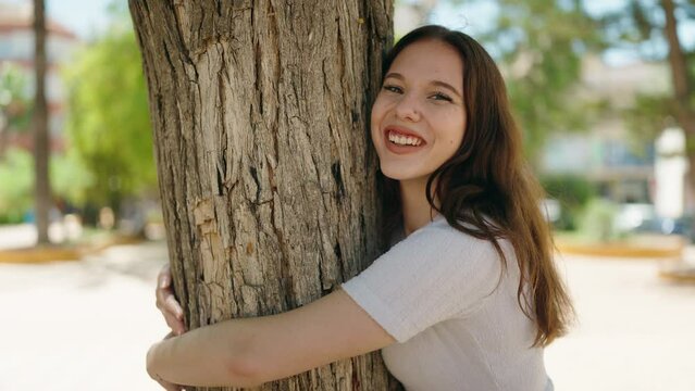 Young woman smiling confident hugging tree at park