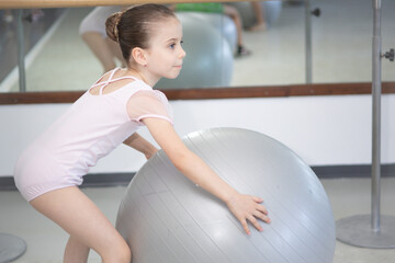 Cute little girl ballerina in a pale pink tutu performs exercises on large ball for gymnastic.