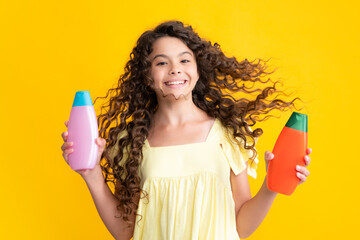 Happy teenager portrait. Teen child girl with shampoo bottle or shower gel isolated on yellow background. Kids hair cosmetic product. Smiling girl.