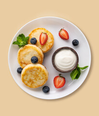 Cottage cheese pancakes with sour cream, mint, blueberries and strawberries  on a yellow background. Healthy and delicious breakfast. Top view