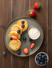 Cottage cheese pancakes with sour cream, blueberries and strawberries on a dark wooden background. Healthy and delicious breakfast. Top view..