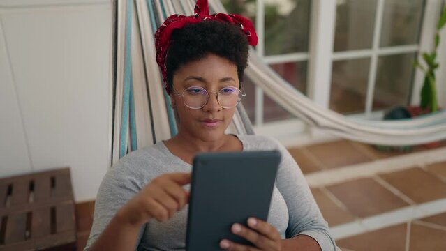 African american woman using touchpad lying on hammock at home terrace