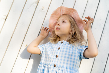 Happy little girl stands by the white wooden wall and smiles