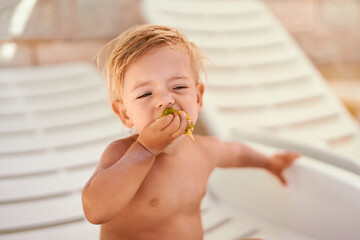 Little girl bites fruit while sitting on a sun lounger in the shade