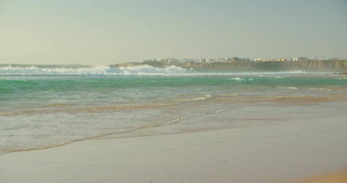 View of El Cotillo city in Fuerteventura, Canary Islands, Spain. Crystal clear ocean huge waves crash and splash on fine empty sand white beach. Scenic cinematic colorful traditional village.