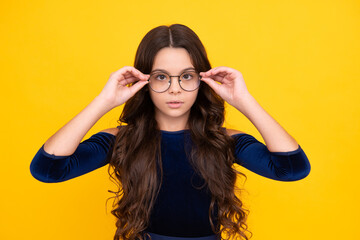 Tennager child girl wear eyeglasses looking at camera with confidence over yellow background, copy space. Kid get eyesight.
