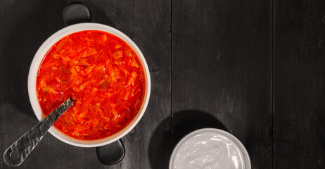 Black plate of borscht on a wooden table, top view. Traditional Ukrainian Russian hot soup. Beets, cabbage, carrots, potatoes, peppers, onions, dill, parsley, tomatoes, in meat or vegan broth. Banner