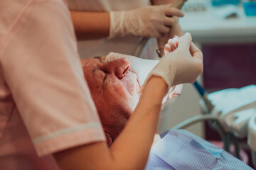 A dentist with the help of a colleague performs an operation on the jaw of an elderly patient in a modern dental clinic
