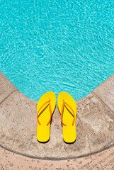 Fototapeta premium Yellow Flip Flops at the edge of a swimming pool deck in the summer with copy space