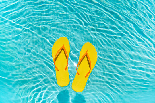 Yellow Flip Flops floating in a clear blue swimming pool water in the summer with copy space