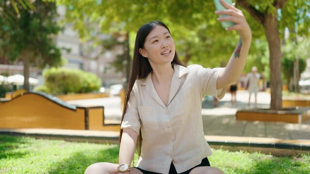 Chinese woman making selfie by the smartphone sitting on grass at park