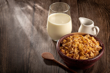 Corn flakes in bowl and glass of milk on table.