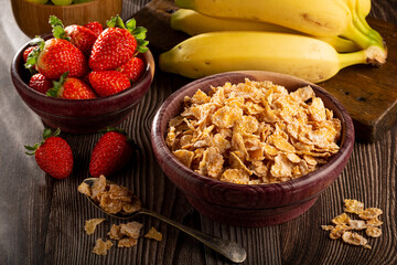 Corn flakes in the bowl with berries on the table.