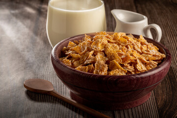 Corn flakes in bowl and glass of milk on table.