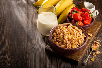 Corn flakes in the bowl with berries and milk on the table.