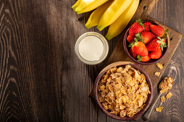 Corn flakes in the bowl with berries and milk on the table.