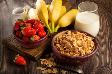 Corn flakes in the bowl with berries and milk on the table.
