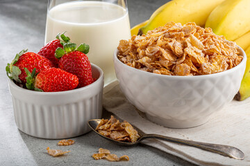 Corn flakes in the bowl with berries and milk on the table.