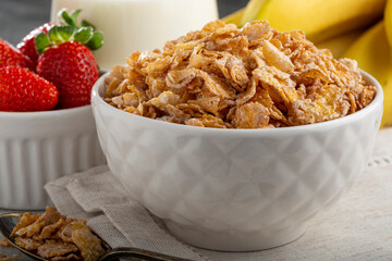 Corn flakes in the bowl with berries and milk on the table.