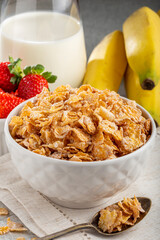 Corn flakes in the bowl with berries and milk on the table.