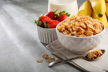 Corn flakes in the bowl with berries and milk on the table.