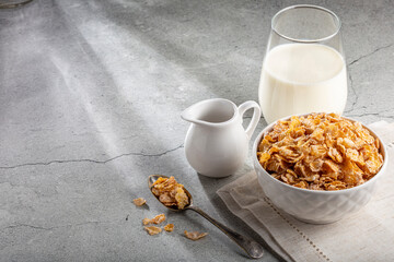 Corn flakes in bowl and glass of milk on table.
