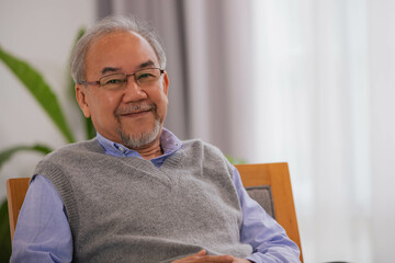 An old man sitting on the sofa in an early morning living room, smiling and happy.