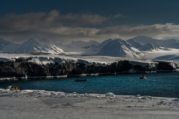 2022-07-15 SNOW COVERED MOUNTAINS AND ICE SHELF WITH SOME EXPOSED ROCK IN A INLET WITH SEVERAL ZODIACS NEAR THE ISLAND OF SVALBARD NORWAY IN THE ARCTIC