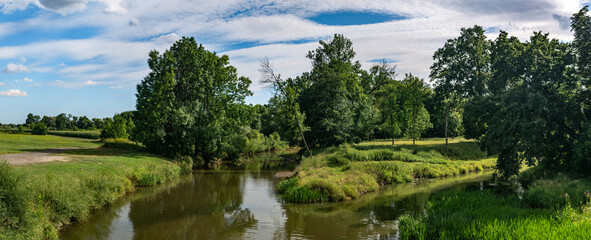 krajobraz rzeki Osobłogi w zachodniej Polsce w jasnych zielono niebieskich barwach i lekko pochmurnej pogodzie - obrazy, fototapety, plakaty