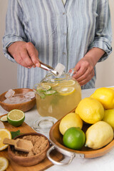 Woman's hands preparing homemade lemonade.  lime, lemon, mint on the kitchen table.