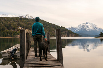 Joven de vacaciones disfrutando junto a su perro de un paisaje único entre lagos y montañas en Patagonia. 