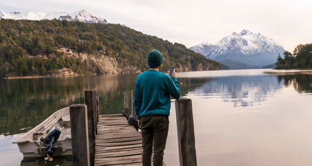 Joven turista sacando fotos con su celular y enviándole  a sus amigos durante un paseo por la Patagonia Argentina, Bariloche, Sudamerica. 