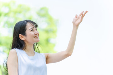新緑の中で笑顔で手をかざす日本人女性
