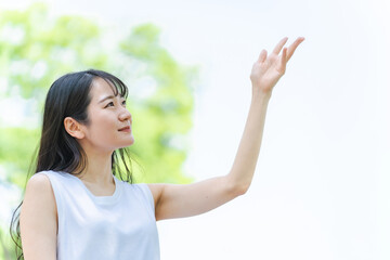 新緑の中で笑顔で手をかざす日本人女性

