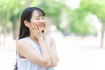 新緑の中でスキンケアする笑顔の日本人女性（美容・美白）
