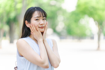 新緑の中でスキンケアする日本人女性（美容・美白）
