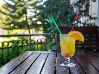 Glass of non alcoholic yellow juice Conga cocktail on table outdoors at tropical resort with palm tree. Horizontal. Healthy fresh cold drink. Vegetarian cocktail party. Copy space