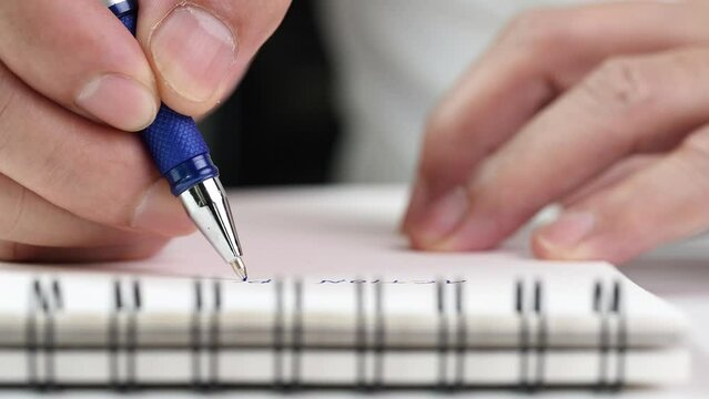 Close up hand writing paper on notebook with blue pen to note, memo, list action plan at office or home desk, selective focus 4k resolution. Concept of write on paper, letter, pen, notepad, diary