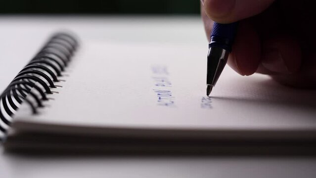 Close up hand writing paper on notebook with blue pen to note, memo, list action plan at office or home desk, selective focus 4k resolution. Concept of write on paper, letter, pen, notepad, diary