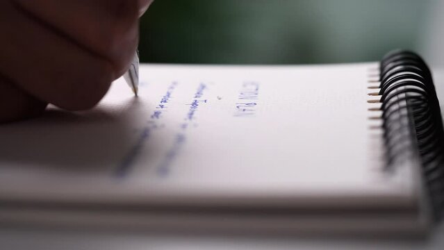 Close up hand writing paper on notebook with blue pen to note, memo, list action plan at office or home desk, selective focus 4k resolution. Concept of write on paper, letter, pen, notepad, diary