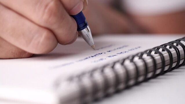 Close up hand writing paper on notebook with blue pen to note, memo, list action plan at office or home desk, selective focus 4k resolution. Concept of write on paper, letter, pen, notepad, diary