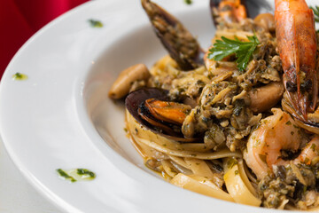 Pasta macarrão italiano em prato branco com fundo vermelho com camarão, lagosta, ostras, bonito, com molho de tomate, com flor de tomate