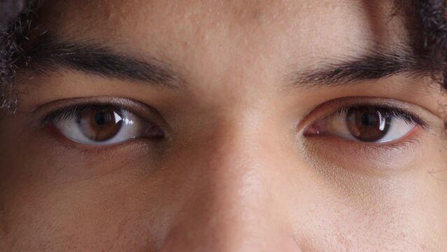 Zoom in on pattern, shape and color of a male gaze, staring confidently with clear, healthy vision. Macro view of a young guy looking motion. Closeup cropped headshot of male brown eyes