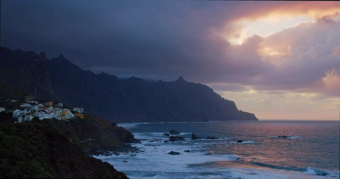 Sunset over Atlantic Ocean, Roques de Anaga. Huge waves form foam and giant volcanic formations in the background. Little village Almaciga in twilight. North of Tenerife. Canary Islands.