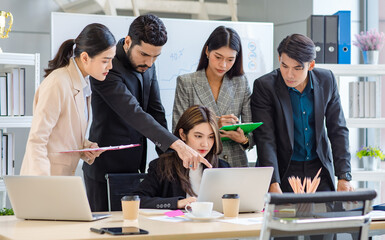 Multicultural multinational millennial Asian female businesswomen Indian male businessman boss in formal suit helping working brainstorming together with laptop computer in conference meeting room