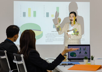 Unrecognizable unknown businesswoman audience in formal suit sitting in conference meeting room holding hand up asking question while Asian female presenter presenting graph chart data on wall screen